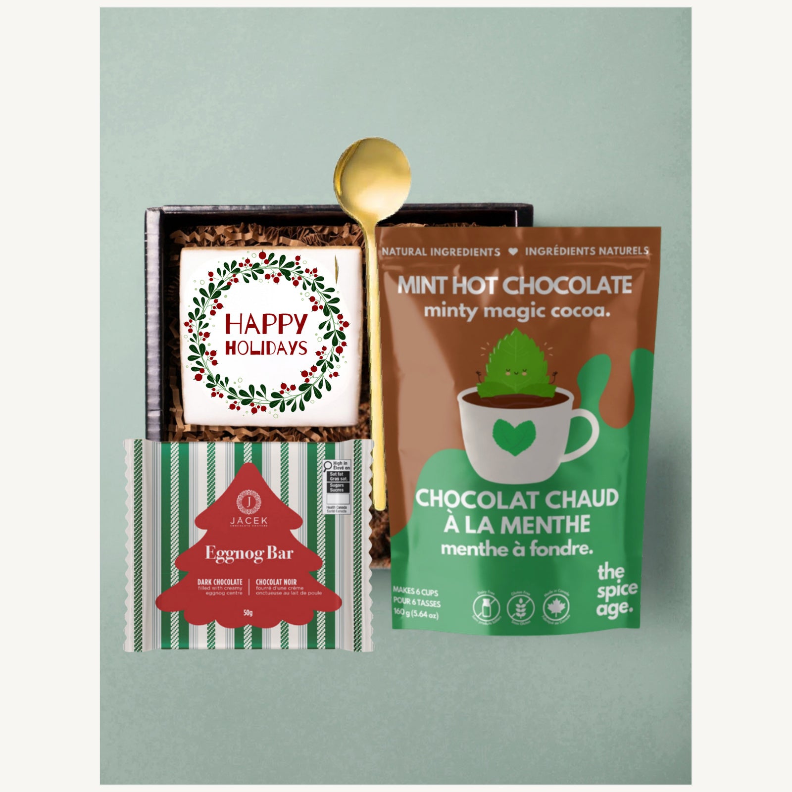 Happy Holidays gift selection with a sugar cookie, JACEK Eggnog Bar, The Spice Age mint hot chocolate and a gold spoon.