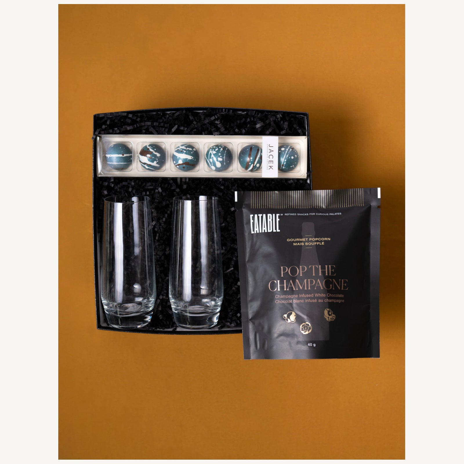 The Cheers gift selection with two champagne glasses, JACEK salted caramels and Eatable Pop the Champagne popcorn.