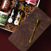 Handmade walnut board and gold butter knife beside Evoolution oils and gourmet condiments.